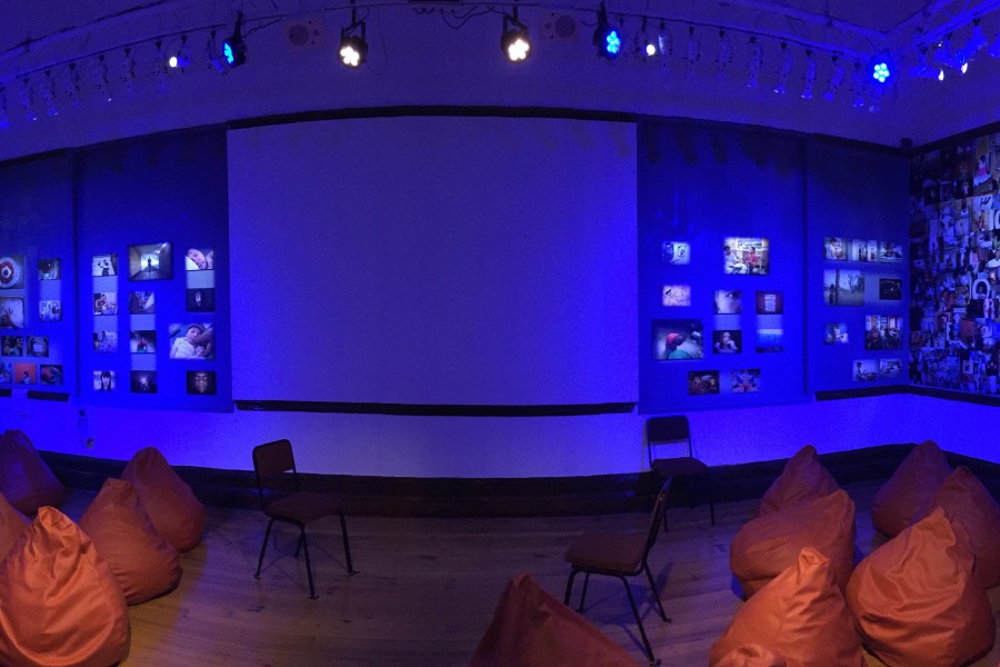 Panoramic Banishing Stigma Room with its projector-screen wall centered among photographic wallpaper and red beanbag chairs