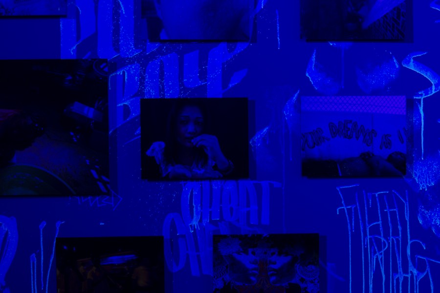 Artivist photographs against a wall with graffiti-like phrases revealed by blacklight