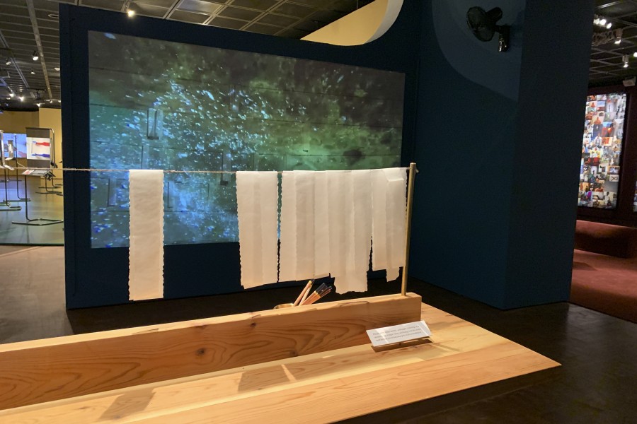 Reflection writing station with hanging paper slips and projected waves of water in the background
