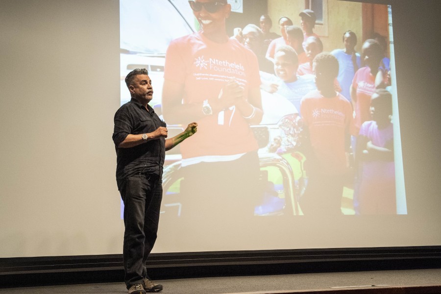 Joey storytelling before an audience with one of his photographs projected behind him