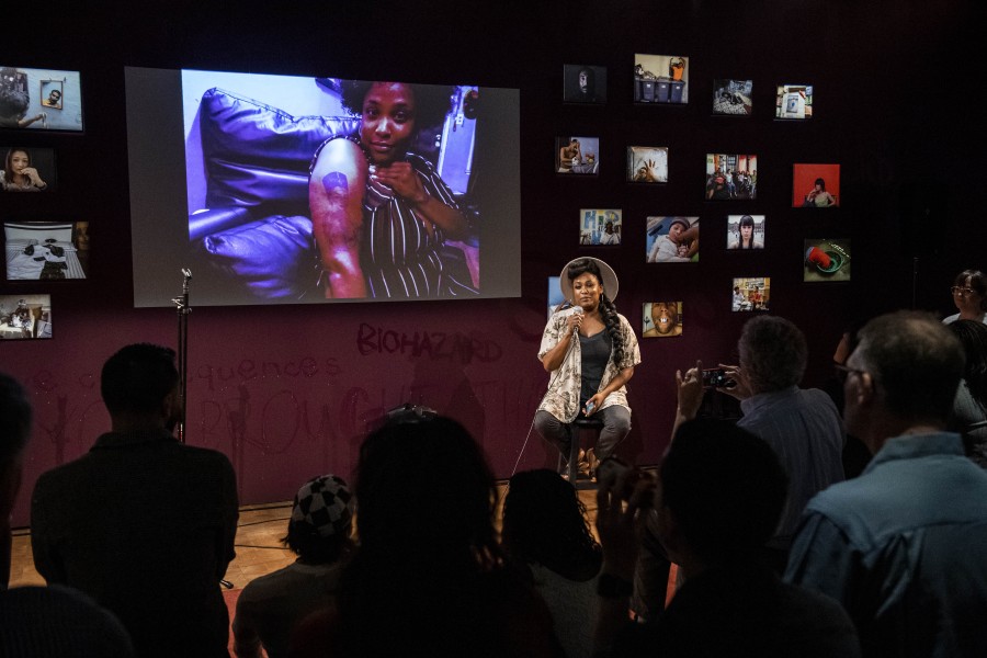 Porchia storytelling before an audience in the Banishing Stigma Room with one of her photographs projected behind her