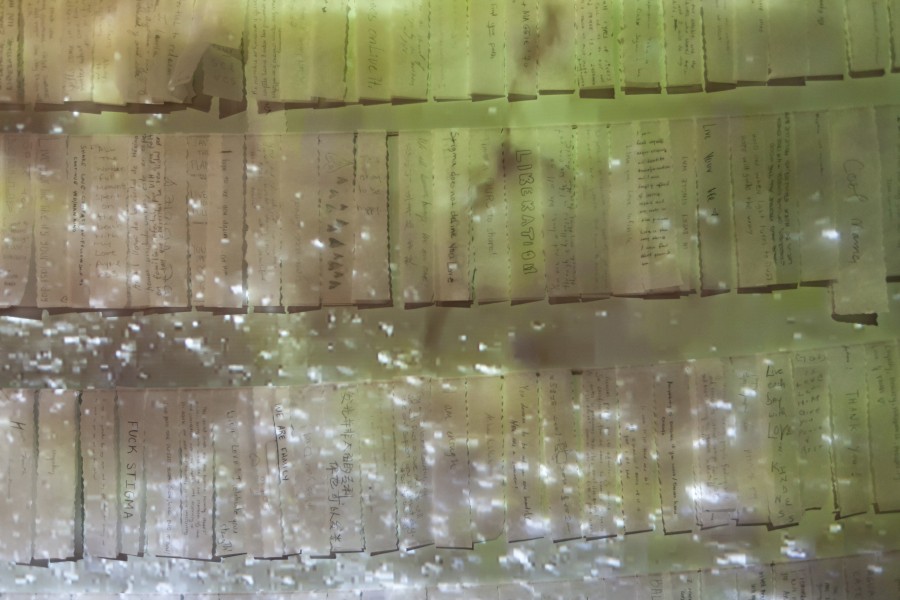 Detail of handwritten notes on hanging paper slips beneath projected waves of water