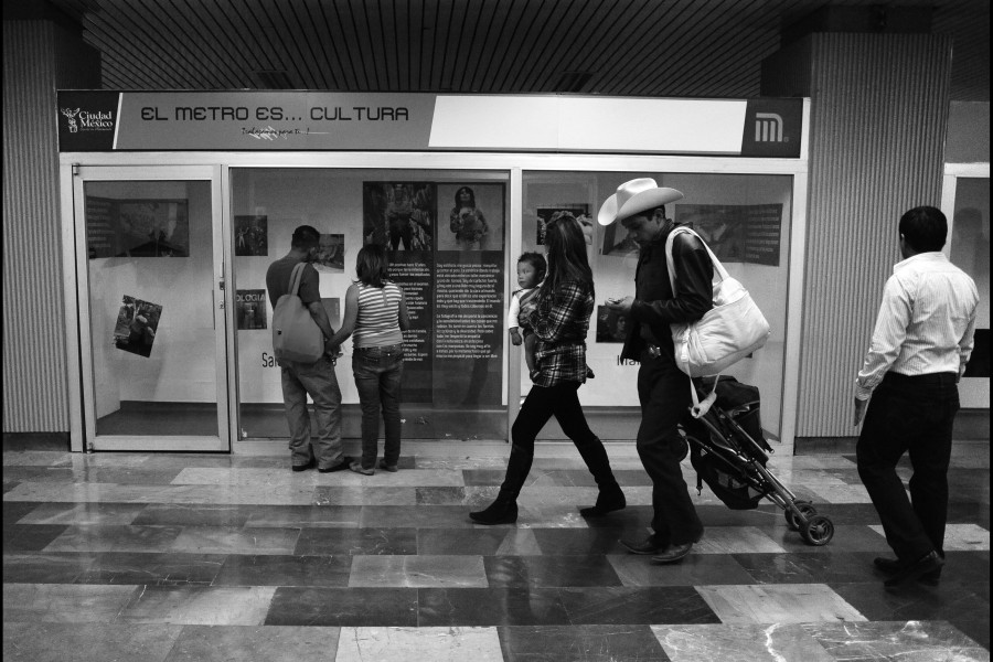 A few people walking past the exhibition while two people stop to view photographs and stories